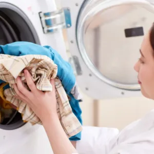 Vrouw stopt kleren in de wasmachine, ze heeft eerder zelf haar goedkope en duurzame wasmiddel gemaakt