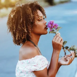 (Zwarte) vrouw ruikt aan bloem en denkt aan zelfzorg en beseft hoe belangrijk dat is in haar rol als moeder