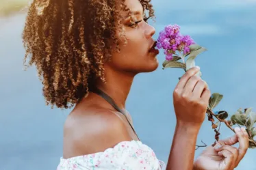 (Zwarte) vrouw ruikt aan bloem en denkt aan zelfzorg en beseft hoe belangrijk dat is in haar rol als moeder