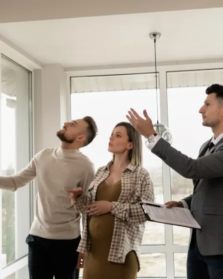 Een koppel: man en een zwangere vrouw bezichtigen of bekijken een woning van binnen en worden geholpen door een makelaar. Zullen ze een huis kopen of toch blijven huren?